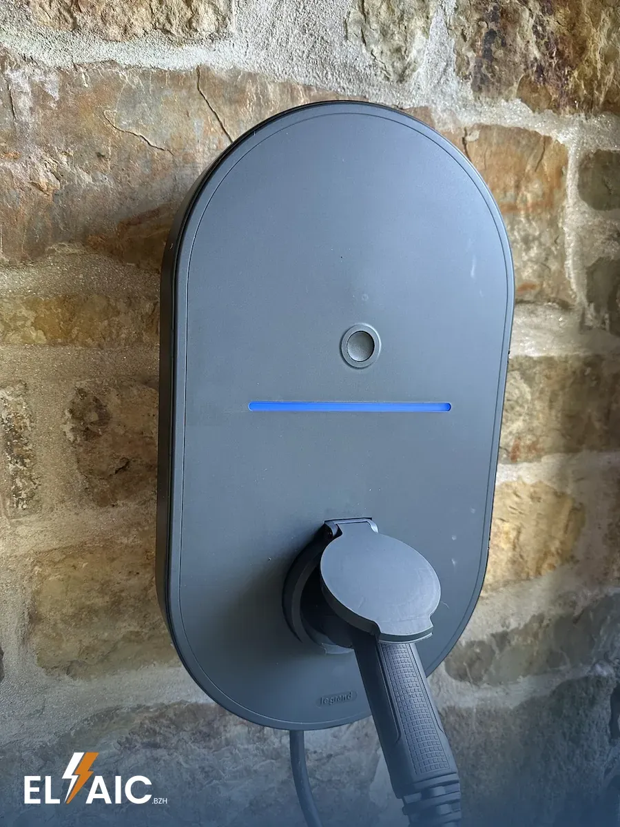 Borne de recharge Legrand Green Up Home fixée sur un mur en pierre, voyant bleu allumé, connecteur branché